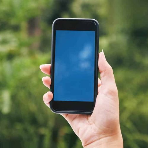 Closeup of a hand holding a cellphone outside in nature. A mobile phone devise in nature. Caucasian.